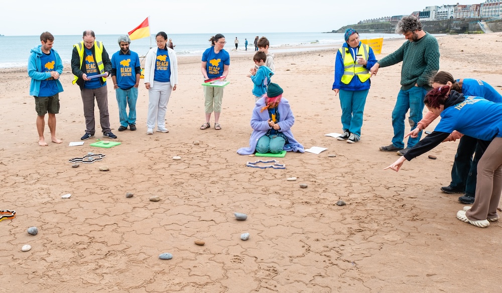 Photo of a team of volunteers wearing Beach Spectres tshirts creating a large tiling on the beach